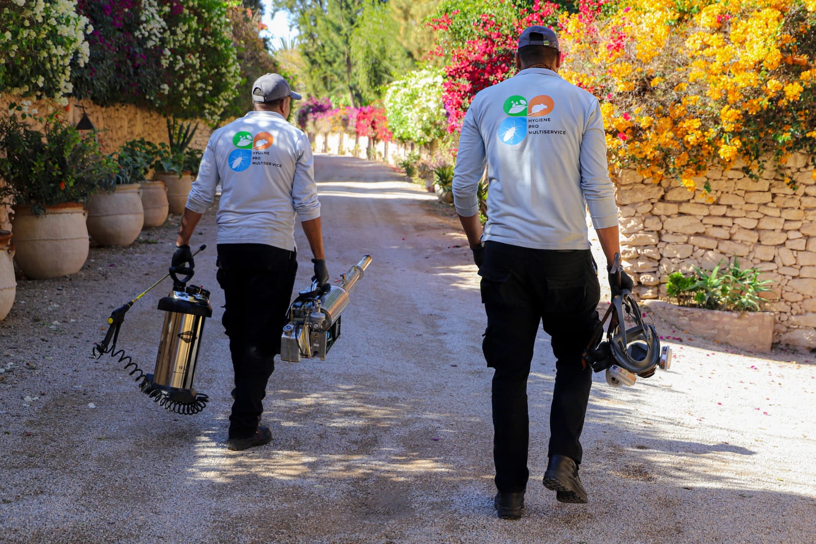 Deux techniciens Hygiène Pro Multiservice en uniforme arrivant sur une intervention, allée fleurie d'un riad à Essaouira